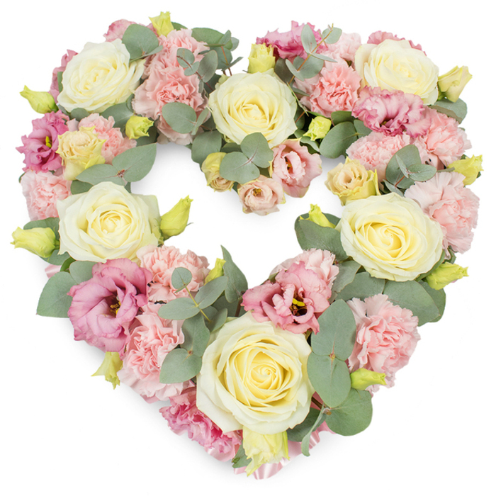 A lavish, heart-shaped wreath of sympathy flowers is presented against a clean white backdrop, capturing the eye with its gentle blend of creams, pinks, and soothing greens. The entire form of the heart is firm yet romantic, built from an abundance of closely set blooms that leave no empty space, only a continuous surface of petals and foliage. Large, fully opened roses in shades of ivory and pale butter yellow act as anchors throughout the tribute, their velvety petals spiralling from tight, structured centres into softly rounded outer edges. Between these roses, clusters of pastel pink carnations fill the spaces, their ruffled petals layering over one another to create a plush, textured surface that feels almost like fabric. Interwoven with this softness are deeper pink to mauve lisianthus flowers, some more open, others still cupping inwards, each adding a gentle wave of colour and a graceful trumpet-like shape. Around and between the blooms, stems of silvery-green eucalyptus curl and fan outward, their round leaves offering a cool, serene balance to the warmth of the pastels and outlining the heart's curves. Small, yellow-green buds appear throughout, hinting at the freshness of the arrangement and suggesting new beginnings even in moments of farewell. The overall mood is one of refined elegance and deep affection, perfectly suited to a funeral, wake, or celebration-of-life service in or around Parsons Green and the nearby Fulham churches. It feels like a tender embrace in floral form, the kind of loving tribute a close family might choose to honour a cherished parent, partner, or friend, allowing their memory to be surrounded by beauty and quiet grace.